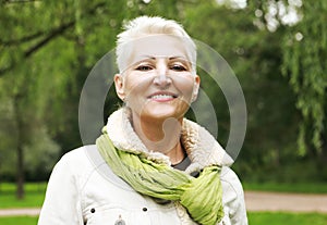 Beautiful blonde woman with blond short hair in a spring park. Elderly happy lady pensioner.