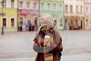 Beautiful blonde woman with cup of coffee using mobile phone