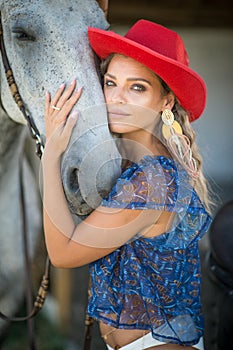 Beautiful blonde woman with curly hair, hat and horse. Portrait of a girl with white bikini blue transparent blouse and her horse