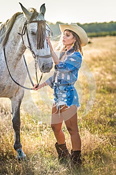 Beautiful blonde woman with curly hair with white hat and horse. Portrait of a girl with denim and her horse.