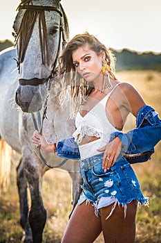 Beautiful blonde woman with curly hair with white hat and horse. Portrait of a girl with denim and her horse.