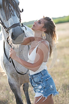 Beautiful blonde woman with curly hair with white hat and horse. Portrait of a girl with denim and her horse.