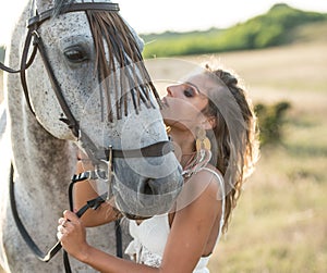 Beautiful blonde woman with curly hair with white hat and horse. Portrait of a girl with denim and her horse.