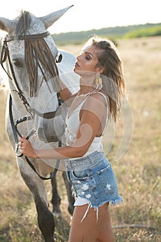 Beautiful blonde woman with curly hair with white hat and horse. Portrait of a girl with denim and her horse.