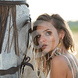 Beautiful blonde woman with curly hair with white hat and horse. Portrait of a girl with denim and her horse.