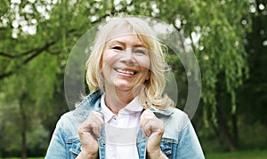 Beautiful blonde woman in a denim jacket in a spring park. Elderly happy lady pensioner. Close up.