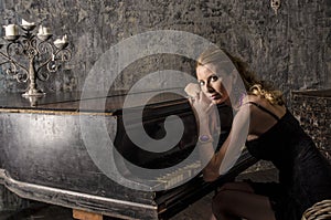 Beautiful blonde woman in an elegant dress at the piano in a dark room