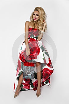 Beautiful blonde woman in an elegant evening gown with red roses, holding a Valentine`s gift, a flowerbox with flowers. Beauty