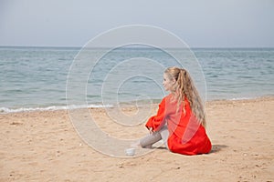 Beautiful blonde woman on an empty beach by the sea drinks