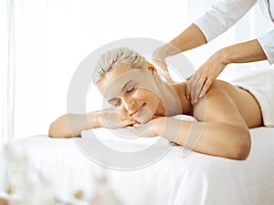 Beautiful blonde woman enjoying back massage with closed eyes. Spa salon concept