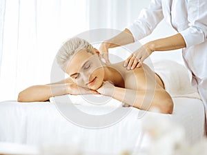 Beautiful blonde woman enjoying back massage with closed eyes. Spa salon concept