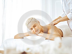 Beautiful blonde woman enjoying back massage with closed eyes. Spa salon concept