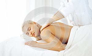 Beautiful blonde woman enjoying back massage with closed eyes. Spa salon concept