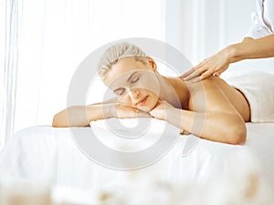 Beautiful blonde woman enjoying back massage with closed eyes. Spa salon concept