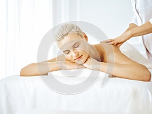 Beautiful blonde woman enjoying back massage with closed eyes. Spa salon concept