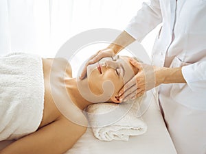 Beautiful blonde woman enjoying facial massage with closed eyes. Relaxing treatment in medicine and spa center concepts