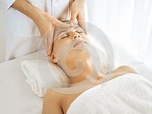 Beautiful blonde woman enjoying facial massage with closed eyes. Relaxing treatment in medicine and spa center concepts