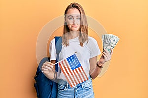 Beautiful blonde woman exchange student holding usa flag and dollars banknotes depressed and worry for distress, crying angry and