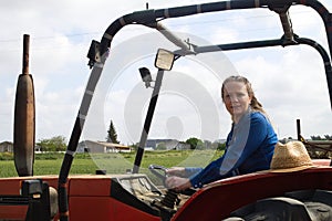 Beautiful blonde woman farmer riding a red tractor to till the soil in order to be able to work in the vegetable garden