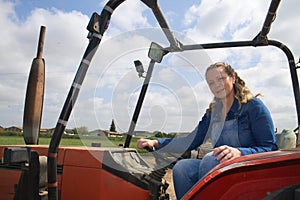 Beautiful blonde woman farmer riding a red tractor to till the soil in order to be able to work in the vegetable garden