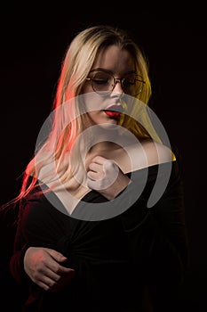 Beautiful blonde woman in glasses wearing blouse with naked shoulders, posing with red and yellow light
