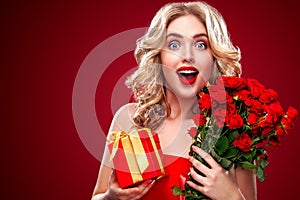 Beautiful blonde woman holding bouquet of red roses and gift. Saint Valentine and International Women`s Day, Eight March