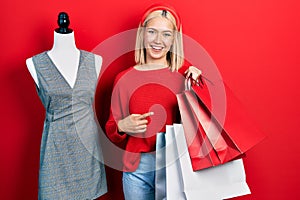 Beautiful blonde woman holding shopping bags smiling happy pointing with hand and finger