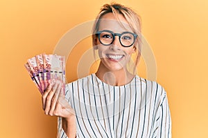 Beautiful blonde woman holding south african 50 rand banknotes looking positive and happy standing and smiling with a confident