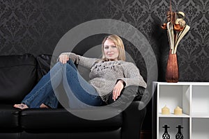 Beautiful blonde woman home on sofa in jumper