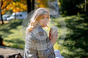 Beautiful blonde woman in light tweed jacket smiles looking over her shoulder at camera. Autumn day in nature. Happiness