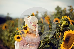 Beautiful blonde woman with long hair and sunhat in a rural sunflowers field outdoors