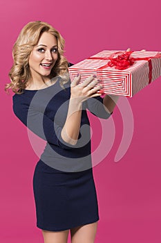 Beautiful blonde woman in luxury blue dress and curly hairstyle holding red present. clear skin. pink background