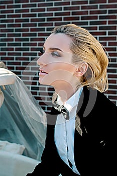 beautiful blonde woman in man black suit with bow tie nearly fountain