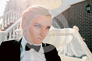 Beautiful blonde woman in man black suit with bow tie nearly fountain