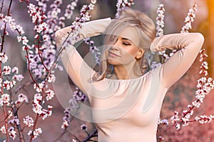 Beautiful blonde woman near blooming pink sakura tree