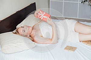 Beautiful blonde woman opens gift in bed in bedroom