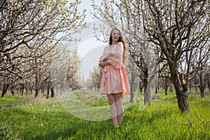 Beautiful blonde woman in pink dress on the road in the flowering garden in spring