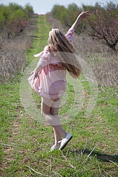 Beautiful blonde woman in pink dress on the road in the garden