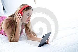 Beautiful blonde woman in pink lingerie wearing headphones holding her tablet and listening to music on white background.