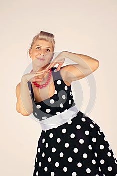 Beautiful blonde woman in pinup style, dressed in a polka dot dress coquettishly looks forward and smiles, white background