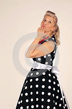 Beautiful blonde woman in pinup style dressed in a polka-dot dress turns around and blows a kiss, white background