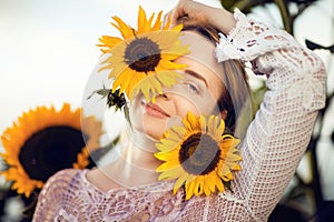Beautiful blonde woman portrait close up, with sunflowers in a rural field outdoors