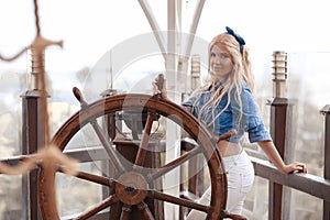 Beautiful blonde woman portrait wears fashion outfit clothes style posing with ship rope by wheel helm