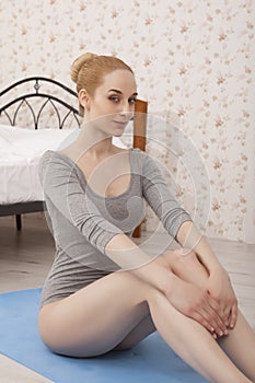 Beautiful blonde woman practicing yoga stretching at home on blue mat in gray bodysuit and pink socks