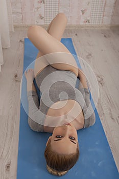 Beautiful blonde woman practicing yoga stretching at home on blue mat in gray bodysuit and pink socks