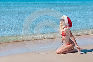 Beautiful blonde woman in red christmas hat and bikini on sea beach