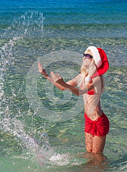 Beautiful blonde woman in red christmas hat on sea beach