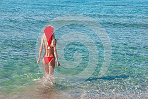 Beautiful blonde woman in red christmas hat on sea beach.