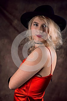 Beautiful blonde woman in red elegant evening dress and black hat.