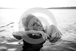 Beautiful blonde woman short hair lies in water on sea shore, pond. Art portrait of a relaxing woman in the water on shore